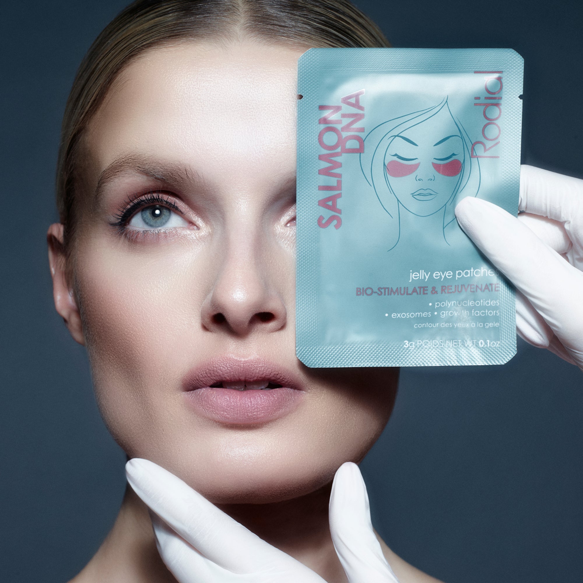 Woman holding a salmon DNA jelly eye patch with a gloved hand against a dark background